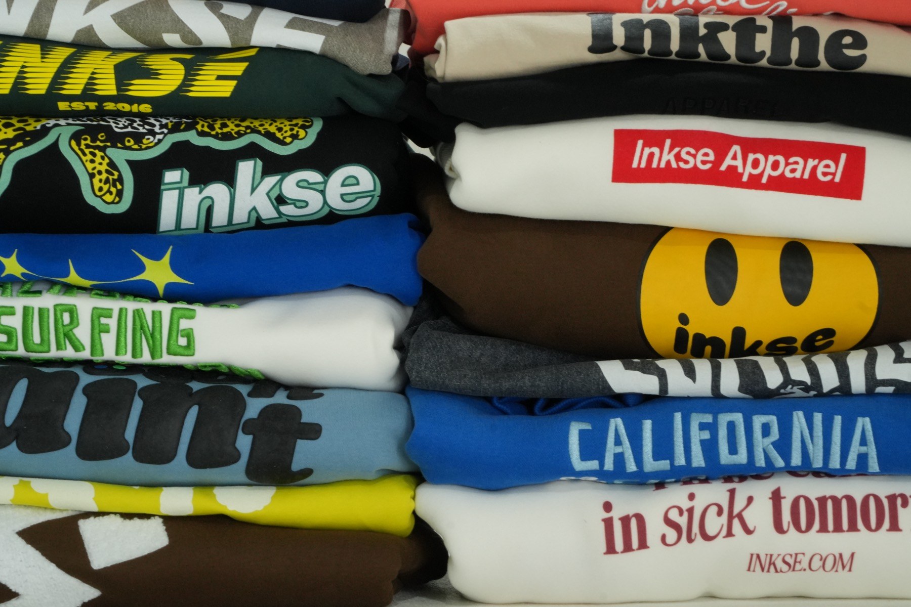 Stack of folded custom tees and sweatshirts showing a range of printed and textured graphics