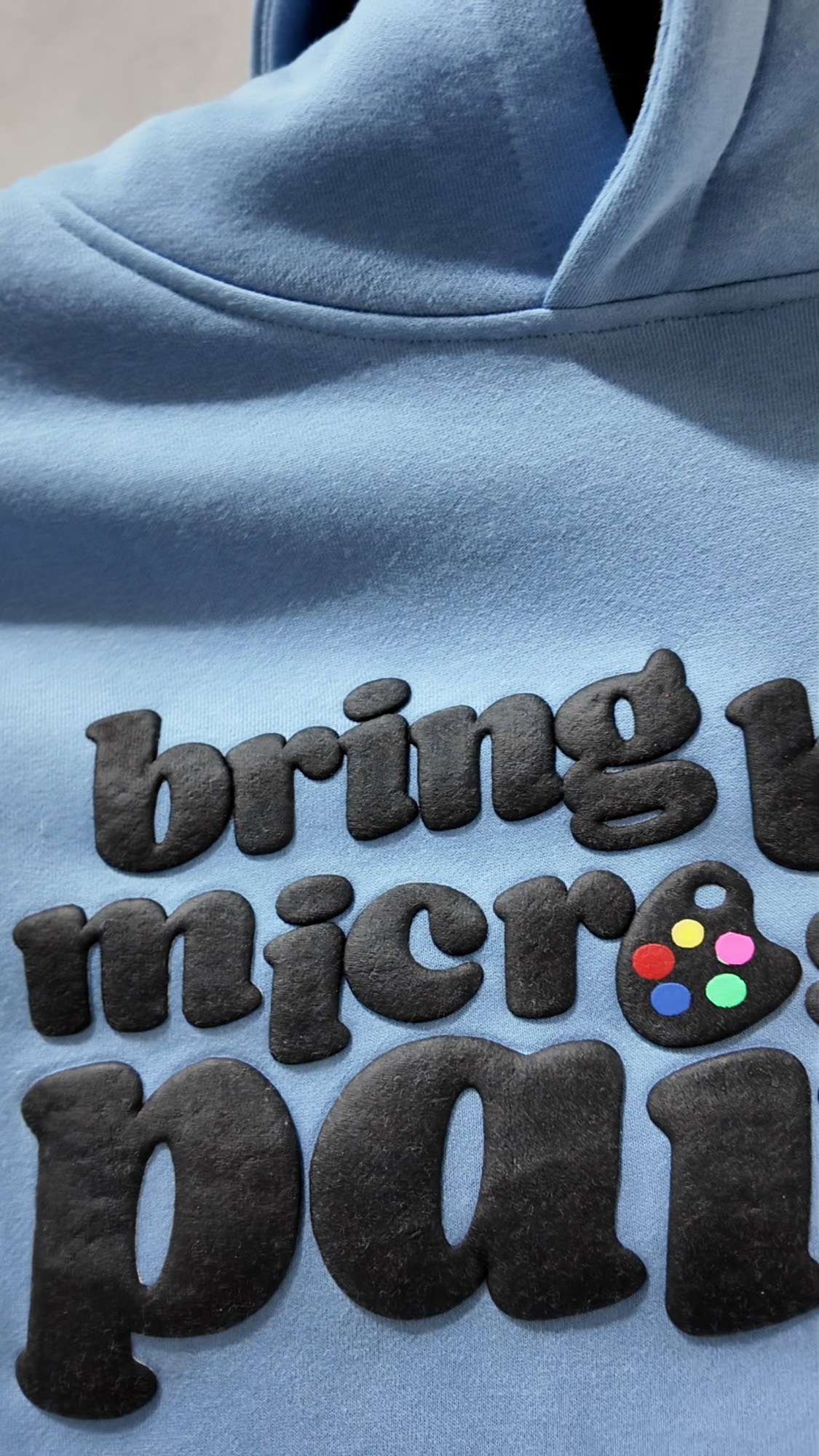 Close-up of black puff print lettering on a light blue hoodie